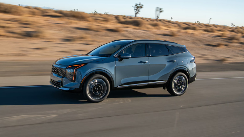 A gray-ish blue 2026 Kia Sportage, in the hybrid configuration, moving at speed down a highway road.