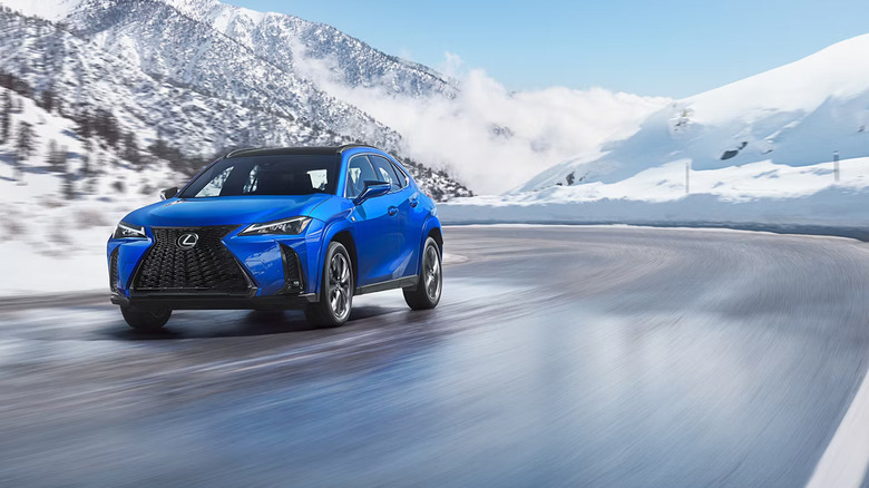 A blue 2026 Lexus 300 series, in the 300h body type, staking a corner while moving on a snowy mountain road.