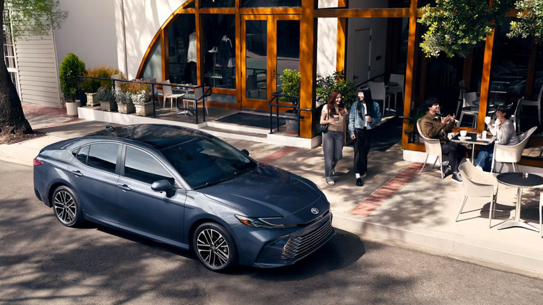 A grayish-blue 2026 Toyota Camry pictured from a top-down view of the right side, standing next to a pavement in a suburban retail neighborhood.