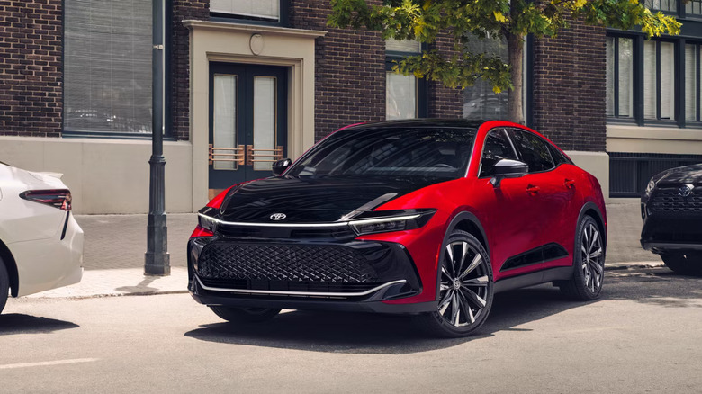 A red and black two-tone 2026 Toyota Crown flagship sedan parked at an angle at the side of a city street.