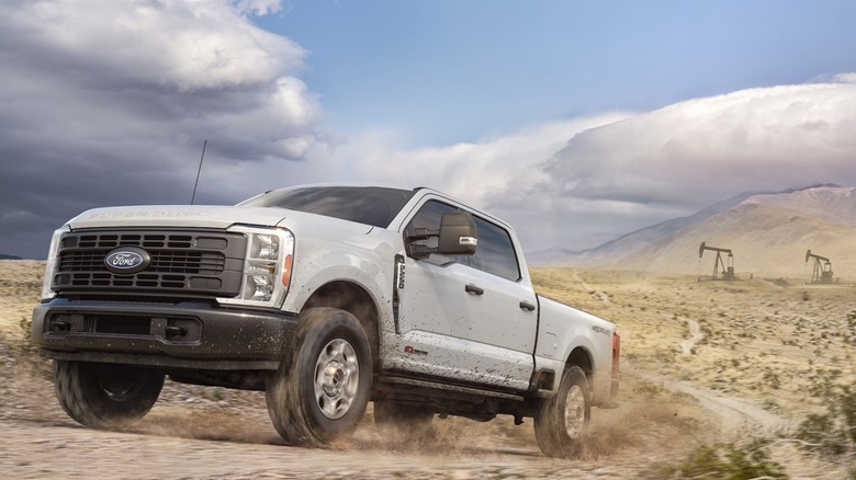 The 2027 Ford Super Duty driving on a remote dirt road, front 3/4 view, flat gray exterior