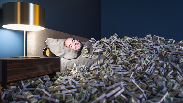 Man lying in bed covered with money