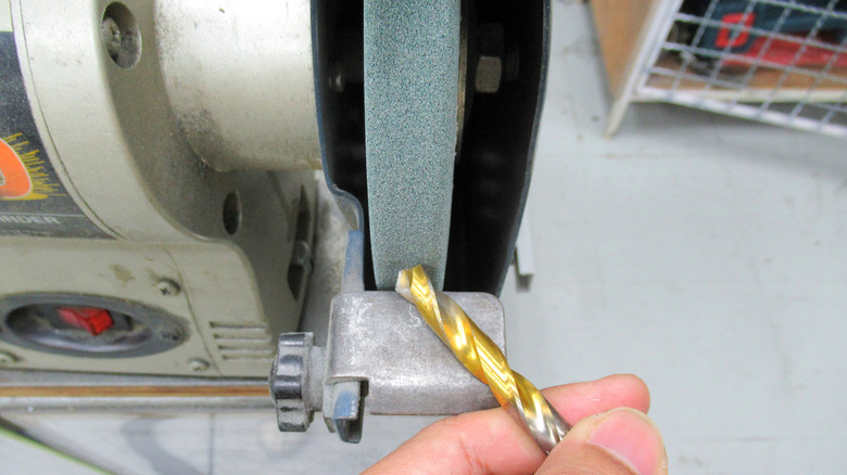 A close up of a man's hand sharpening shiny drill bits with a bench grinder