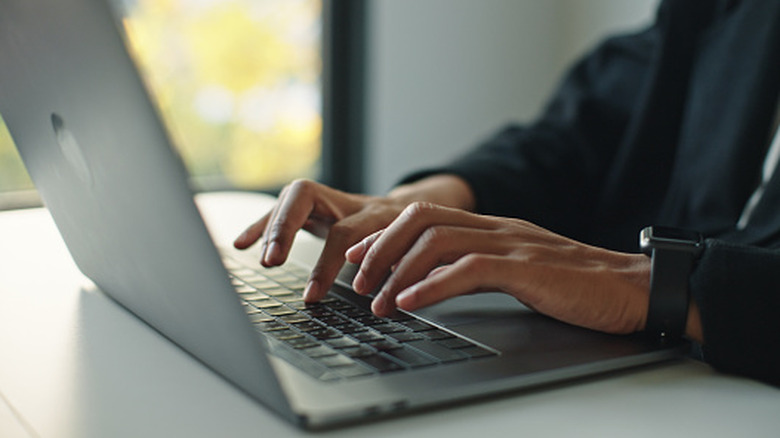 A person typing on a gray laptop