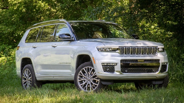 White Jeep Grand Cherokee L parked on grass with trees in the background.