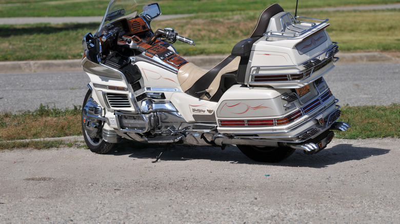 A beige Honda Gold Wing motorbike parked near a lawn.