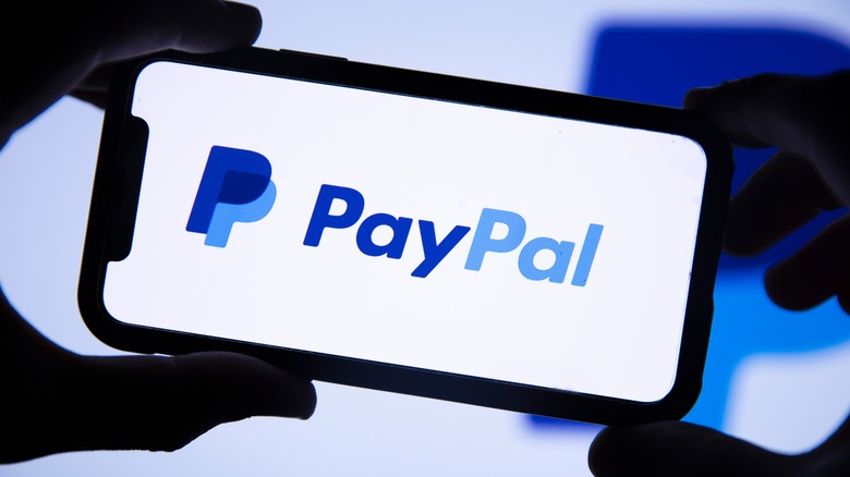 segurando o telefone com o logotipo do PayPal na tela
