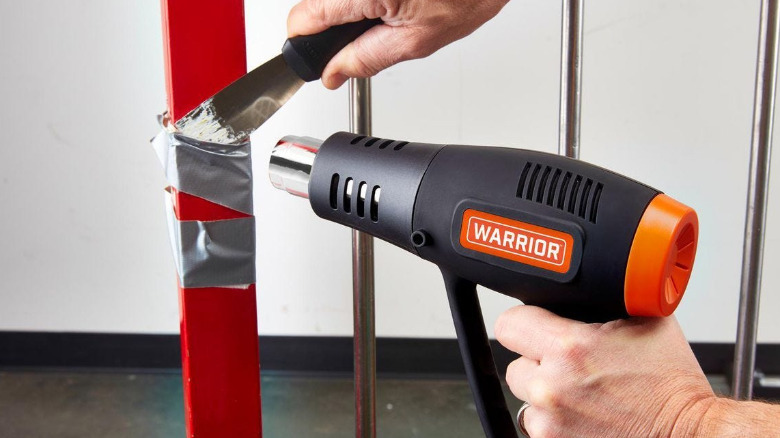 A Warrior heat gun and a paint knife being used to remove duct tape.