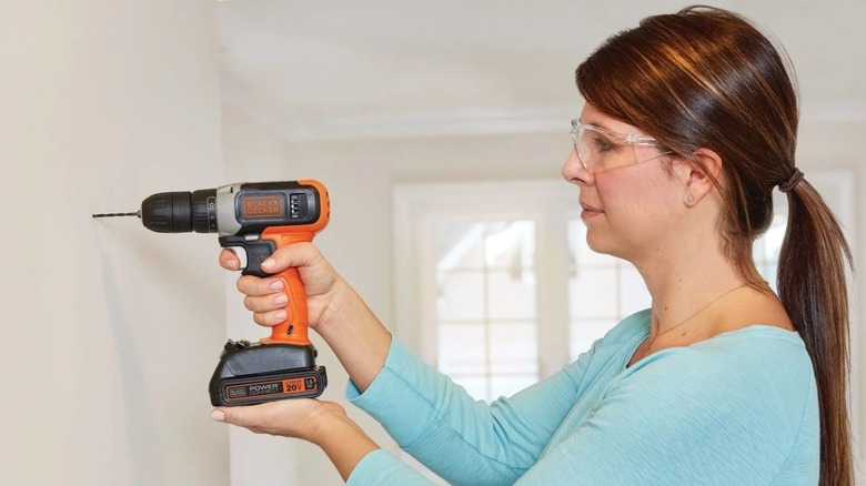 A woman drilling a hole on a wall with a BCD702C1 cordless drill.
