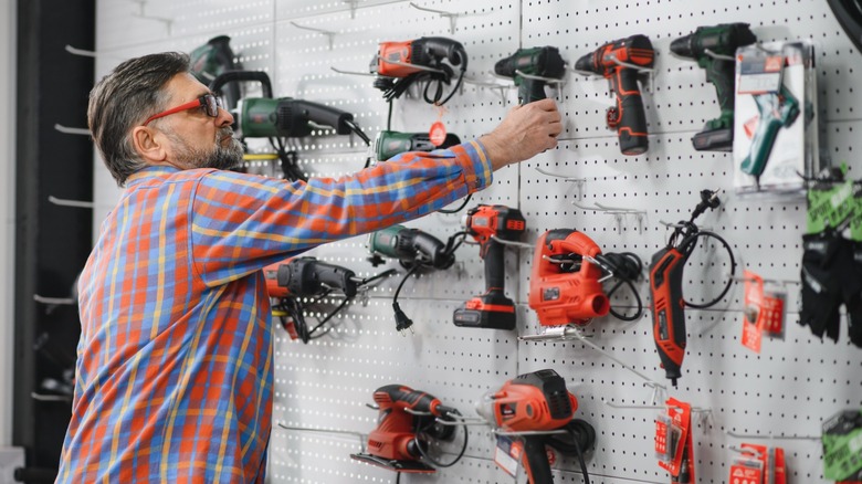 A man picking a cordless drill from a group of drills on display.
