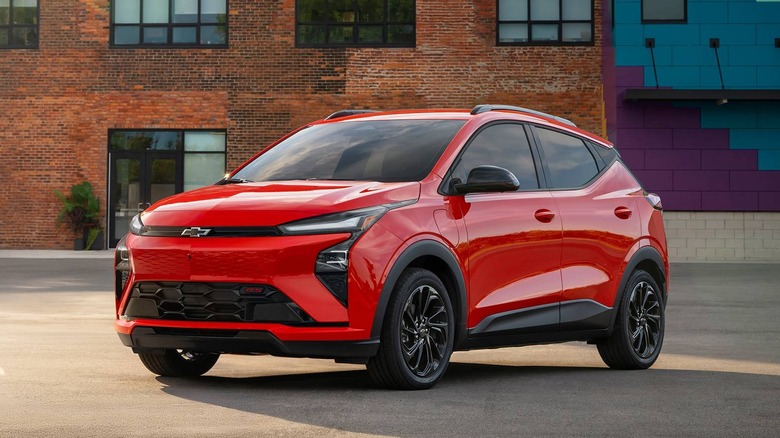 A red 2027 Chevrolet Bolt parked in front of a brick building