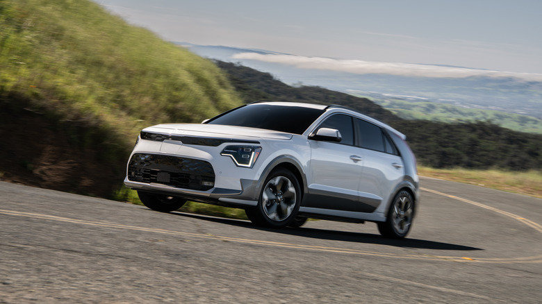 A white 2026 Kia Niro driving uphill on a country road
