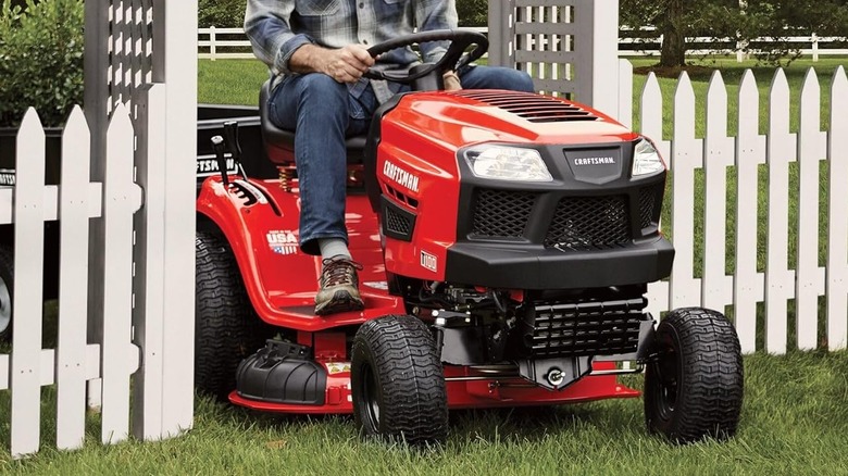 man riding lawn mower through gate