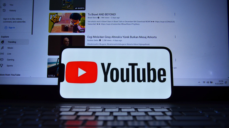 A smartphone showing the YouTube logo on the screen, YouTube's home page in the background.