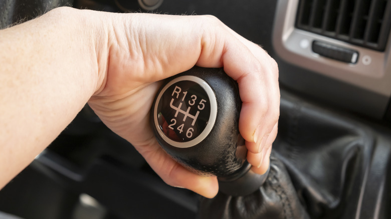 A person's hand gripping the gear shift on a six-speed manual transmission