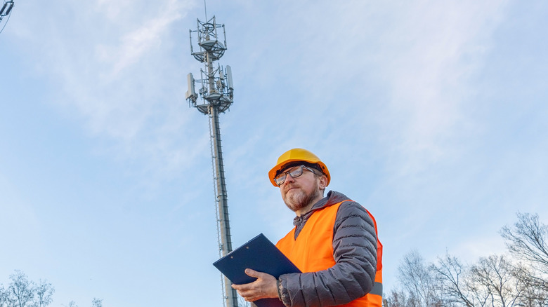 A worker standing with a clip board with a 5G tower in the background