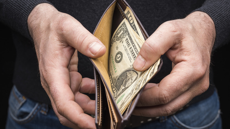 A person holding a wallet and pulling out U.S. dollar bills