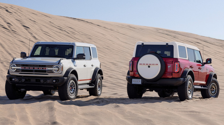 2026 Ford Bronco Anniversary Package shown in Wimbledon White and Ruby Red side-by-side on sand dunes, front and rear-views