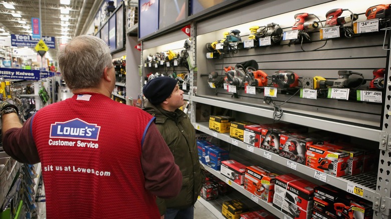 A Lowe's associate helping a customer with a power tool purchase.