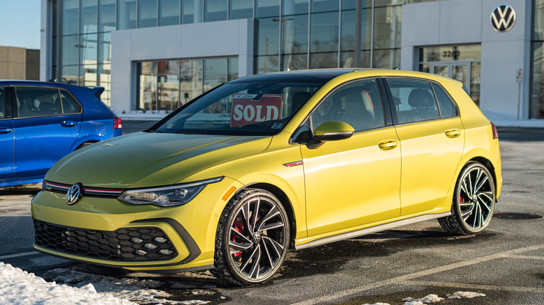 A yellow Mk8 VW Golf GTI parked in front of a snowy VW dealership.