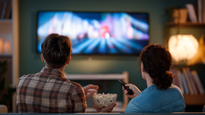 Two persons watching TV seen from behind, the TV is out of focus.