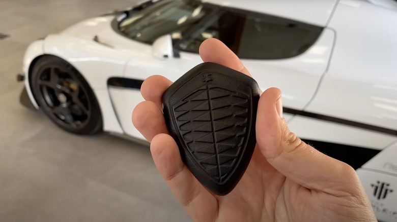 A person holding the Koenigsegg crest key in black, next to a white Regera