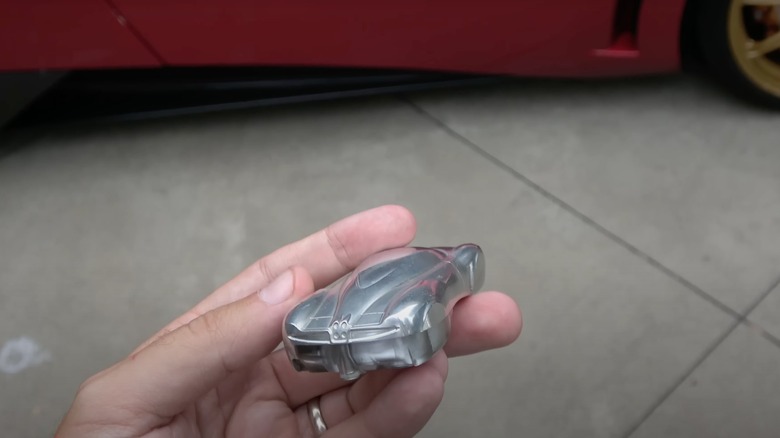 A person holding the Pagani Huayra key fob next to a red Huayra