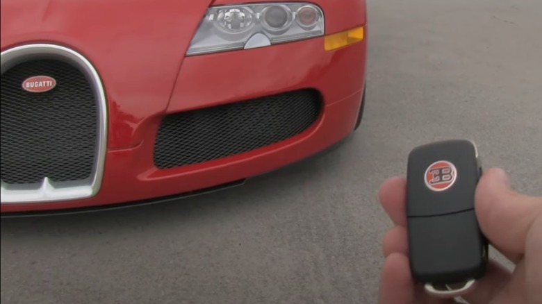A person holding the Bugatti Veyron spare key next to a red Veyron