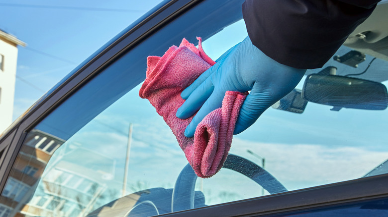 A person using a microfiber cloth on a car's driver-side window.