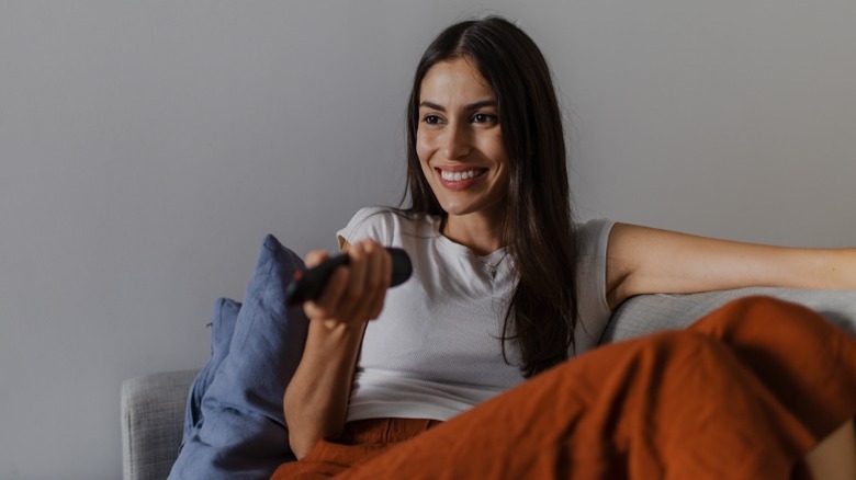 Woman smiles as she points remote at TV