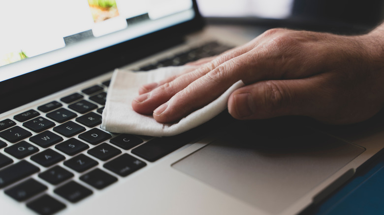 A hand wiping laptop keyboard with cloth