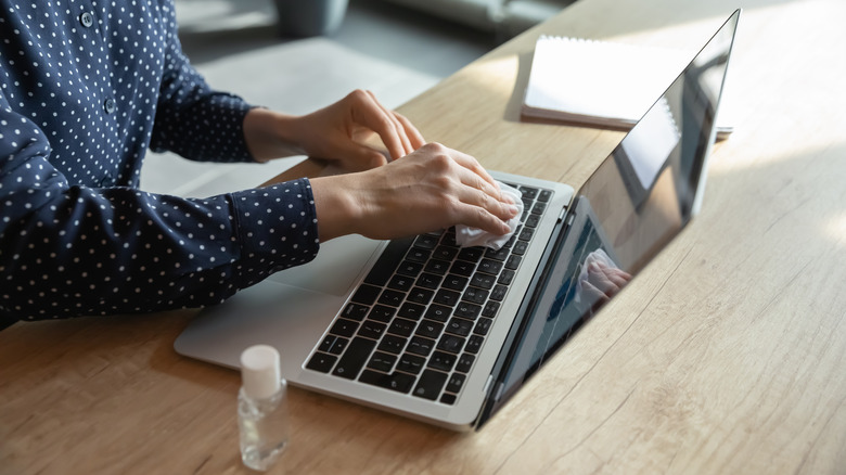 A person wiping down their laptop keyboard.