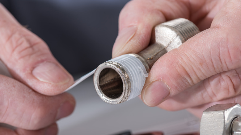 A close-up shot of the plumber's hands putting a teflon joint on a thread.