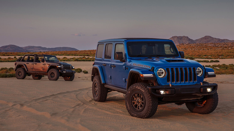 Dark grey and blue colored Jeep Wranglers standing in sand.