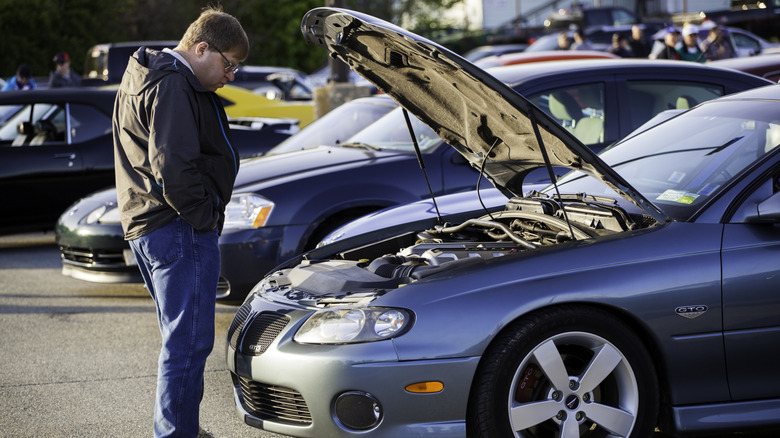 A person looking under the hood of a Pontiac GTO