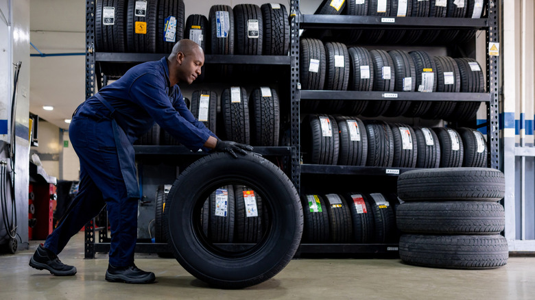 Mechanic rolling tire away from rack of tires.
