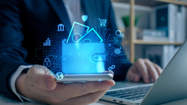 Person holding phone with one hand and typing on computer with other hand, as digital wallet graphic hovers above phone.