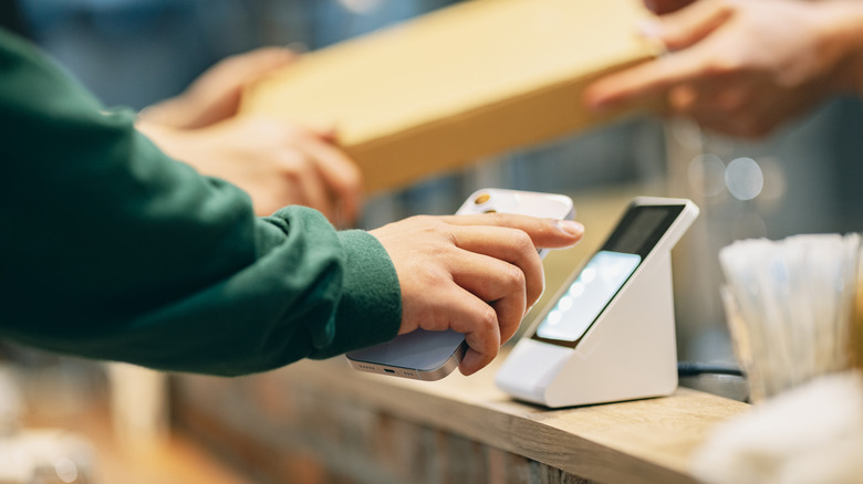 Hands tapping phone to payment device.