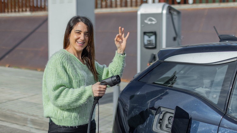 Woman giving OK sign with fingers preparing to charge EV