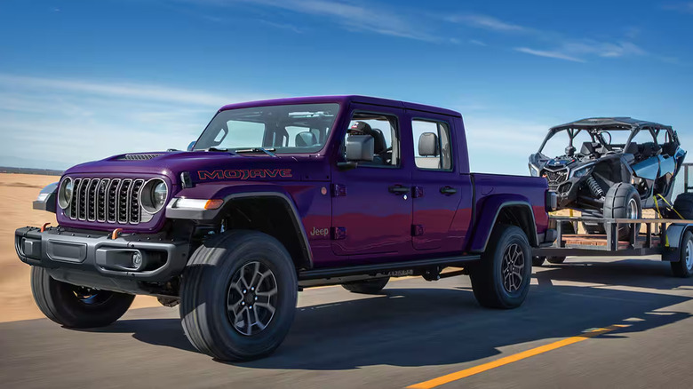 A purple Jeep Gladiator towing a dune buggy on a desert road
