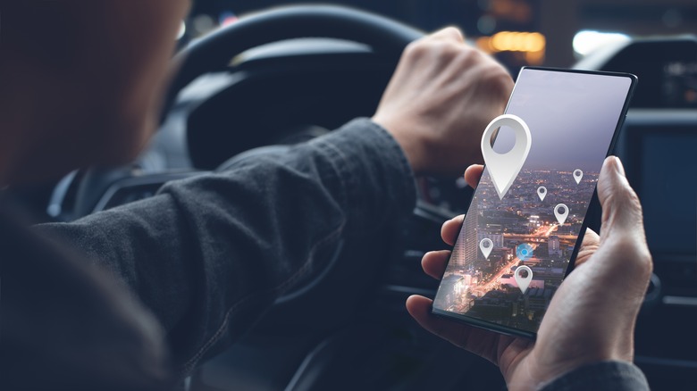 A man sits in a car holding a phone displaying map icons