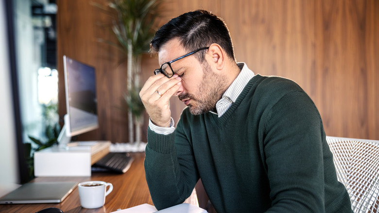person experiencing fatigue and rubbing eyes in front of a work desk