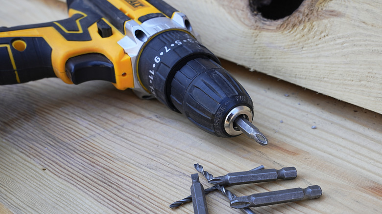A DeWalt drill on a wood table next to several drill bits.