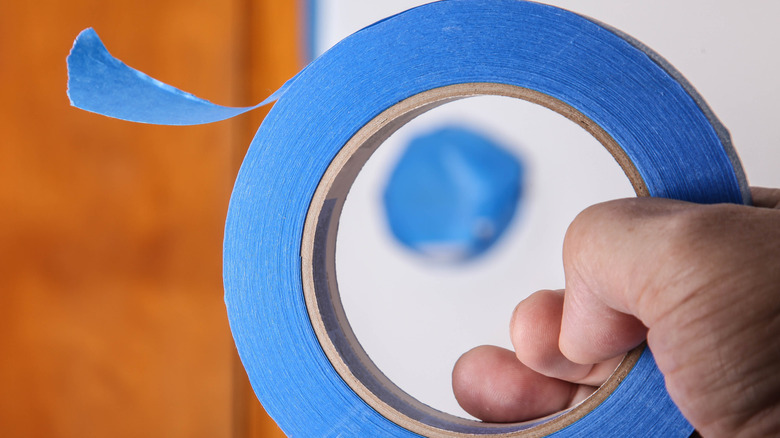 A person holding a roll of blue tape.
