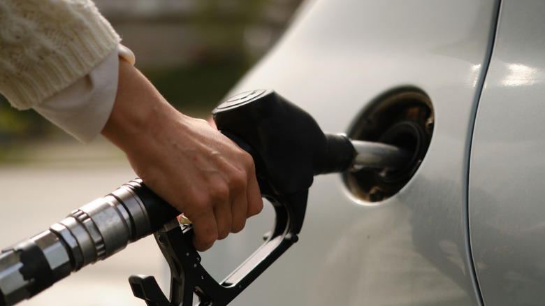 A hand on a fuel nozzle during refueling of car.