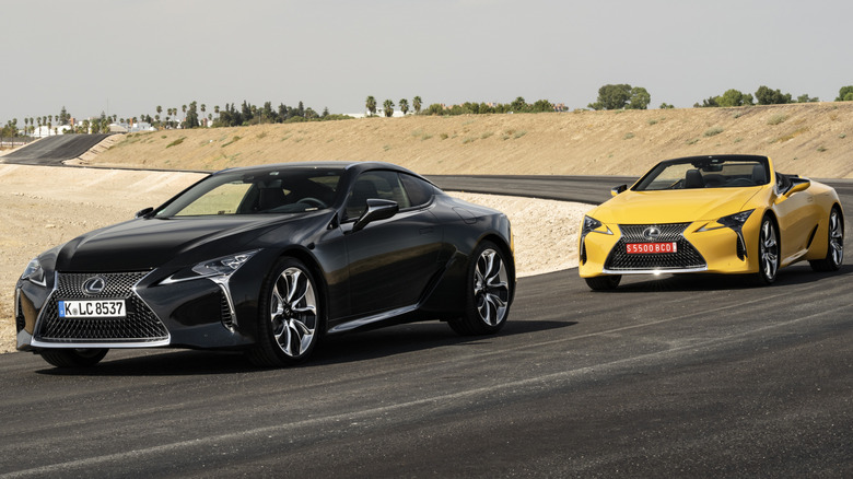 A black Lexus LC500 coupe and yellow convertible parked on a track.