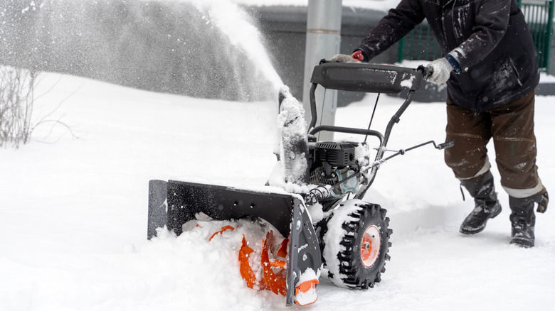 Person operating snow blower in heavy winter snow.