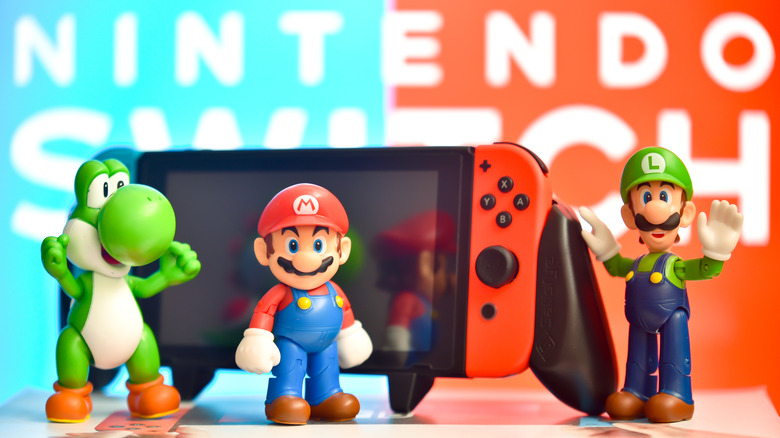 Mario, Luigi, and Yoshi figures in front of a Switch Console