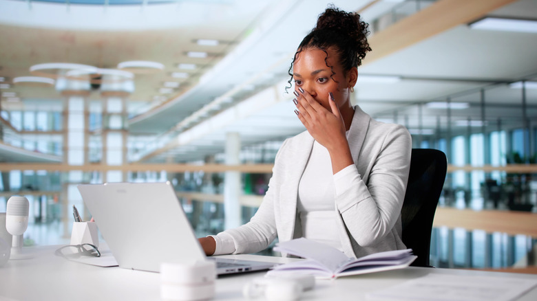 A woman seated at a desk in front of a laptop, gasping as her personal data is exposed in a cyberattack ransomware breach