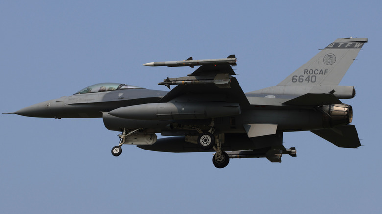 Grey fighter flying with its landing gear down against a clear blue sky.